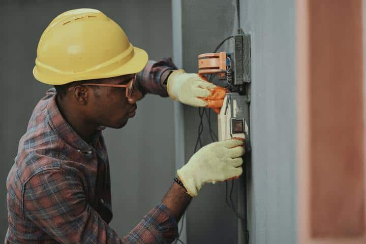 A black man handling with a light box, wearing hardhat, eye goggles and protective gloves.