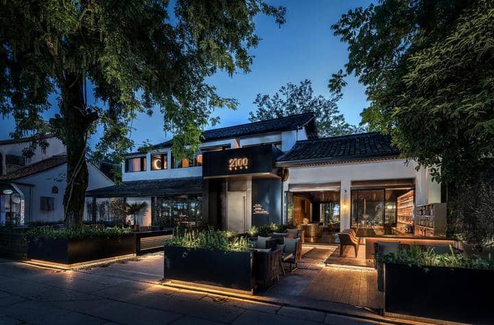 Two-floor club house in the evening with lighted front yard and two entry paths with chairs outdoor