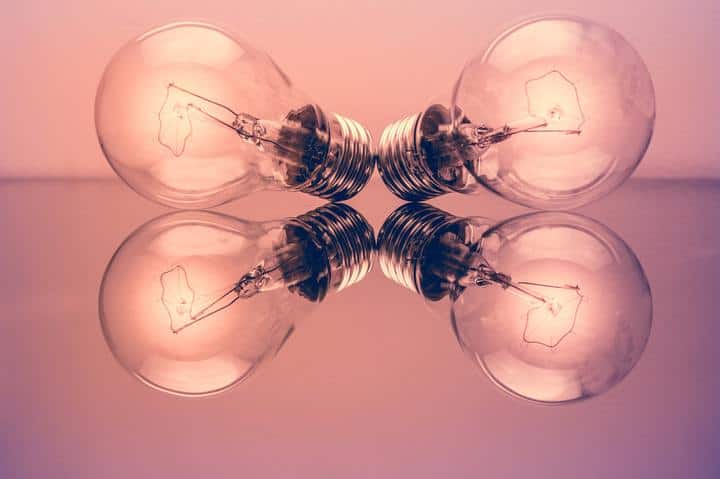 two light bulbs with their reflection on a pink background