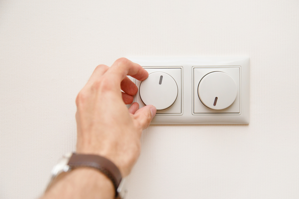 Human hand turning down electrical light dimmer switch.