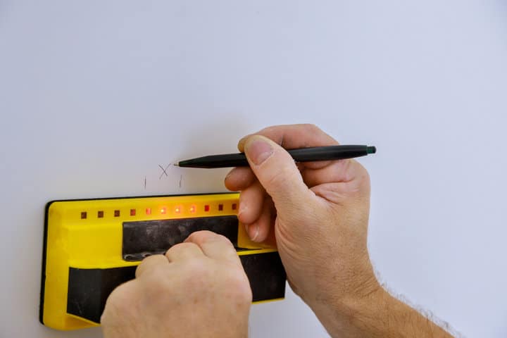 man hand is scanning wall with stud finder